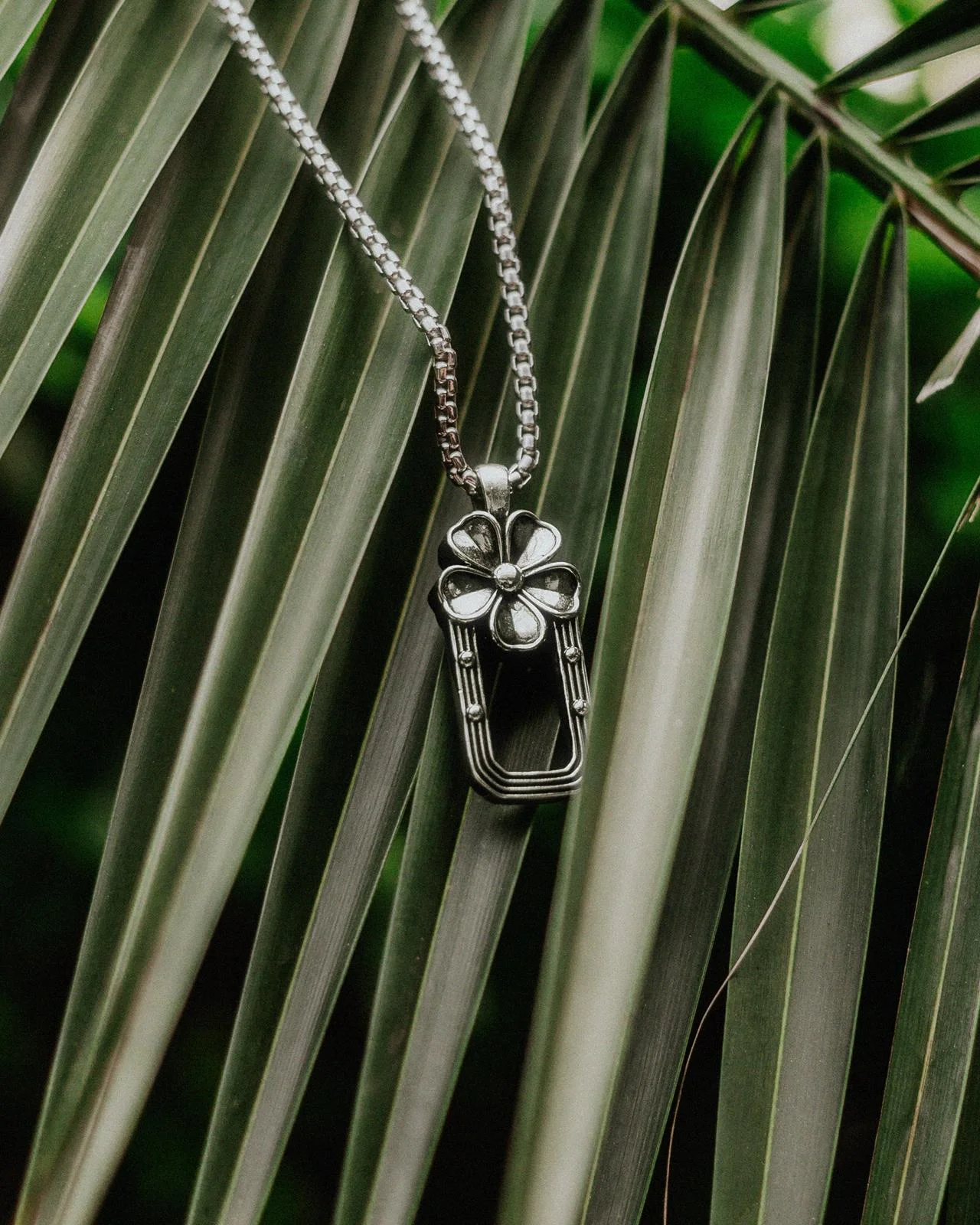 Arch Necklace with a silver flower and open arch pendant against palm leaves.